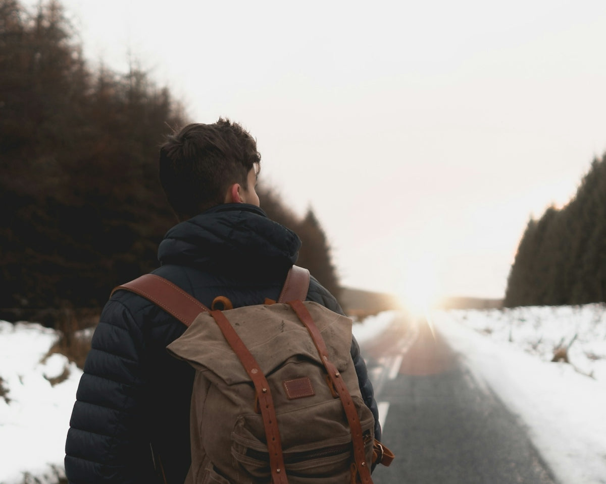 man with backpack standing in middle of road at daytime