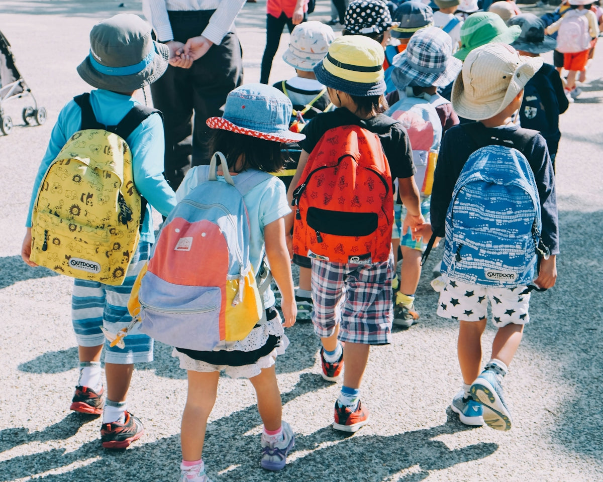 group of people wearing white and orange backpacks walking on gray concrete pavement during daytime