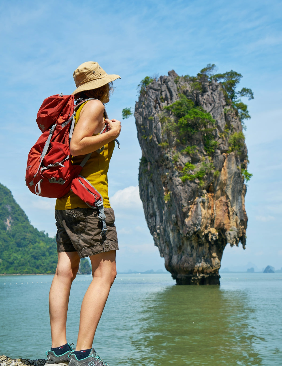 woman in yellow and red tank top and brown shorts standing on rock formation near body