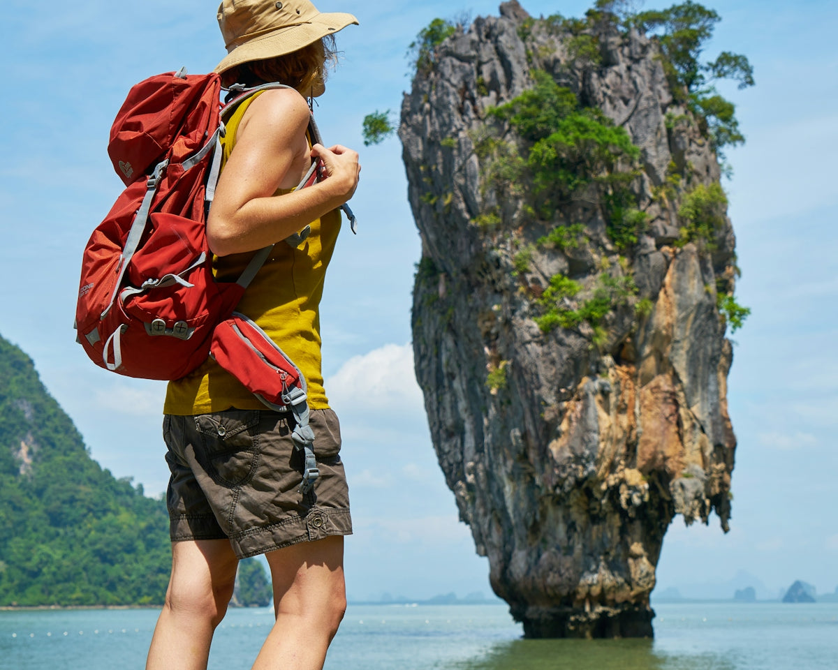 woman in yellow and red tank top and brown shorts standing on rock formation near body