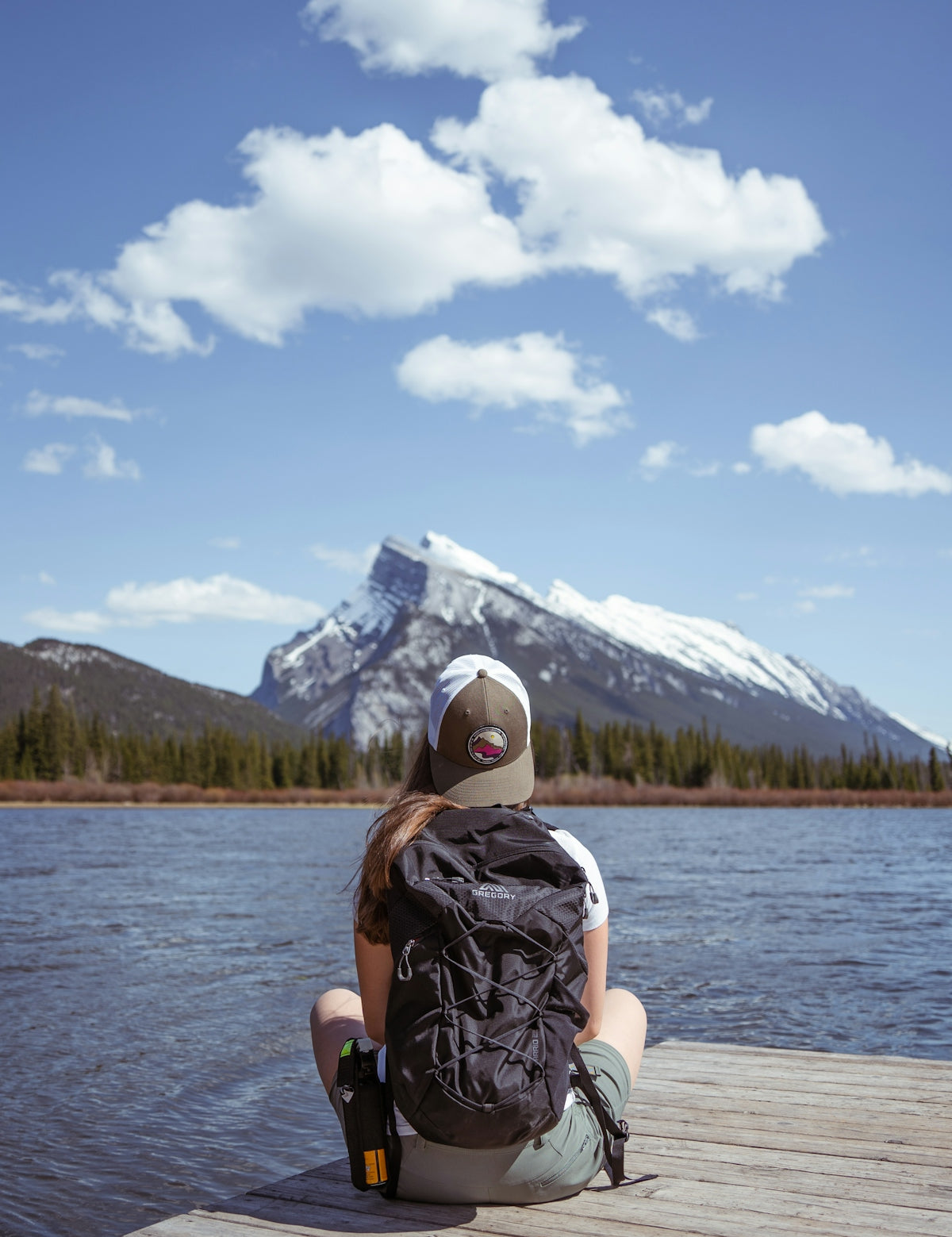 person in black and white backpack sitting on white wooden dock during daytime