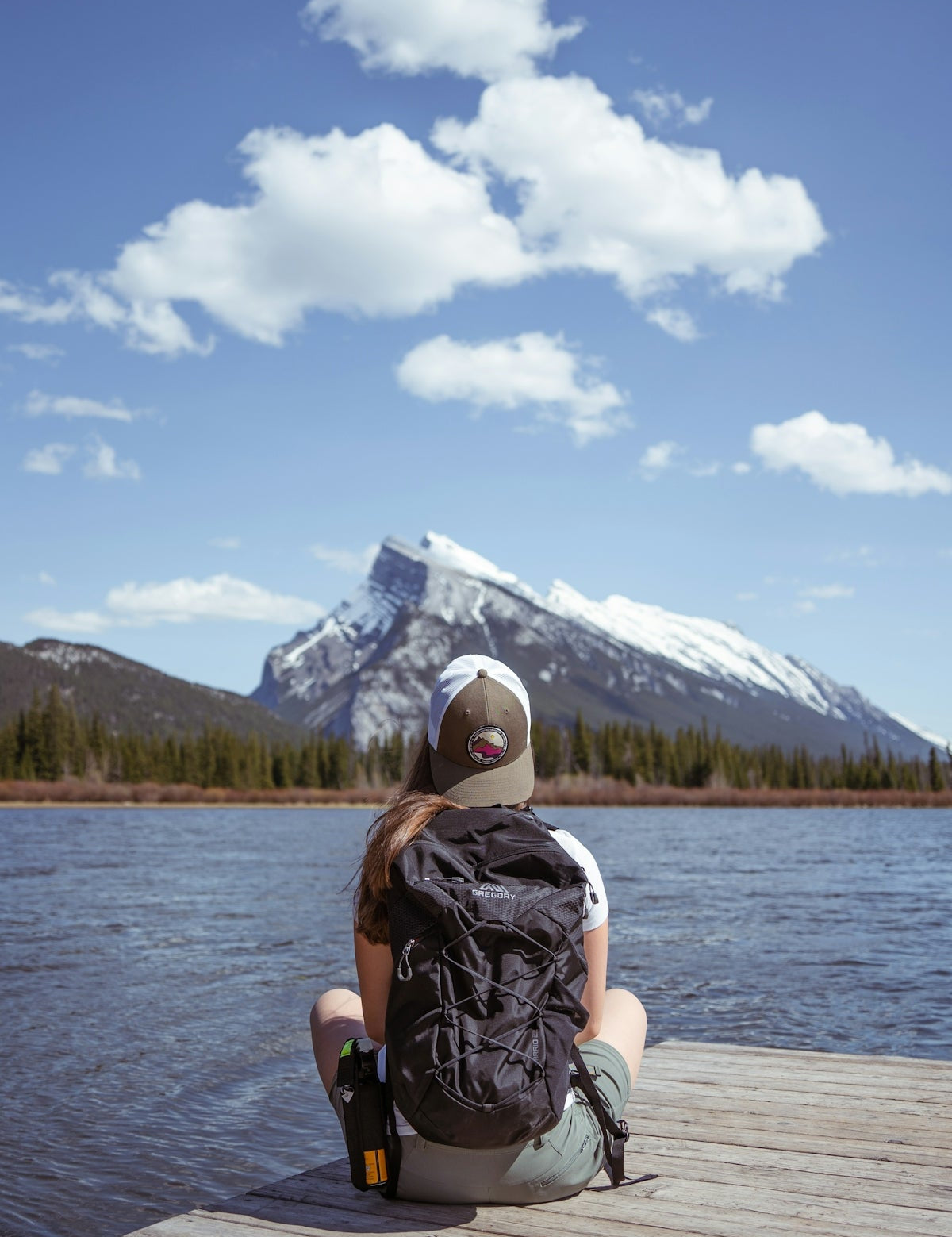 person in black and white backpack sitting on white wooden dock during daytime