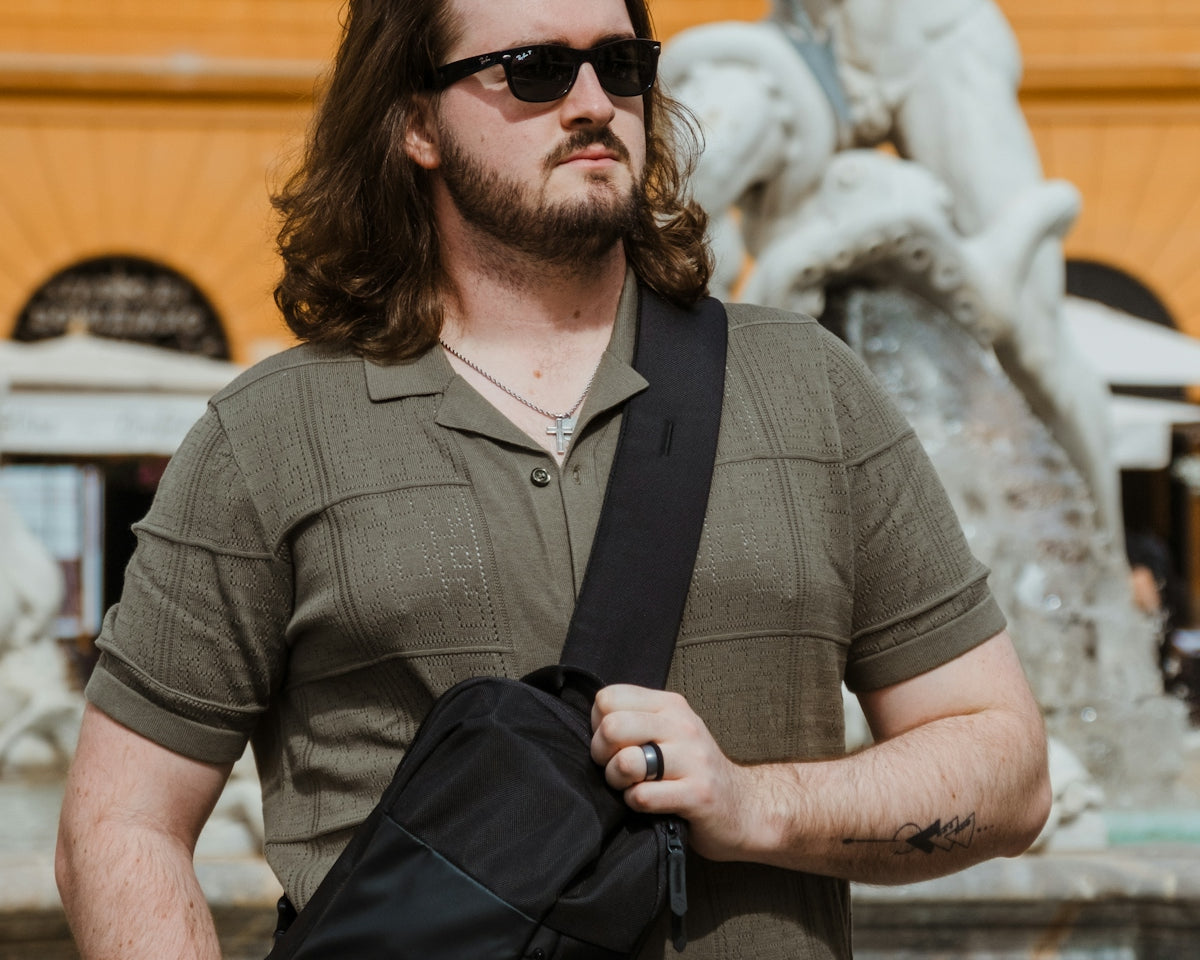 a man standing in front of a fountain holding a black bag