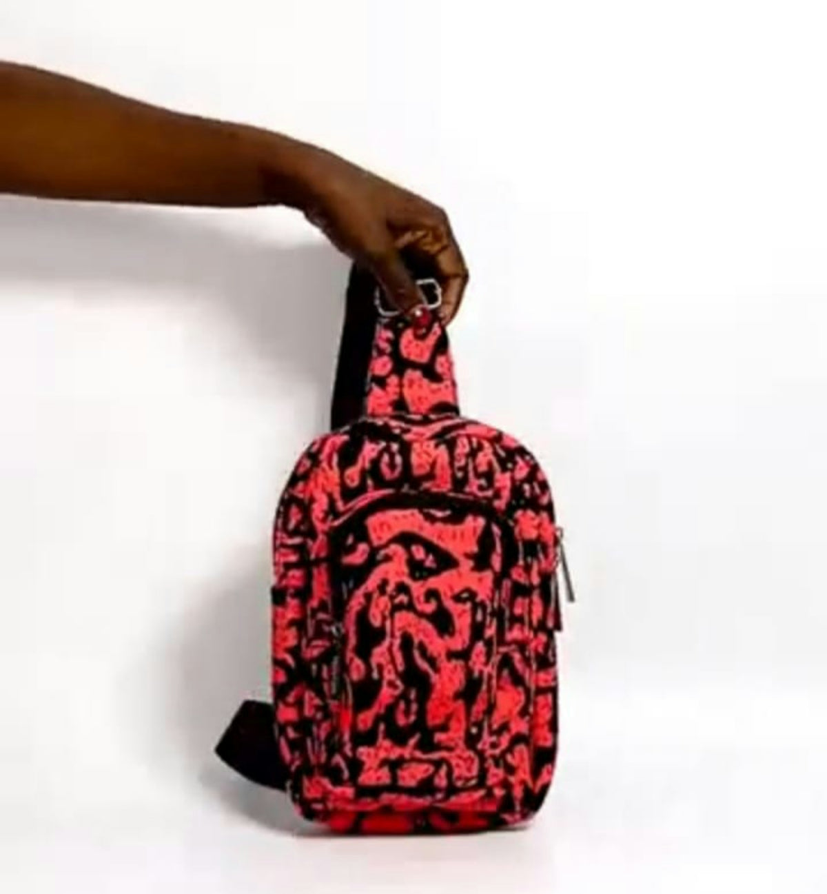 Hand holds a sling bag with a red and black pattern.