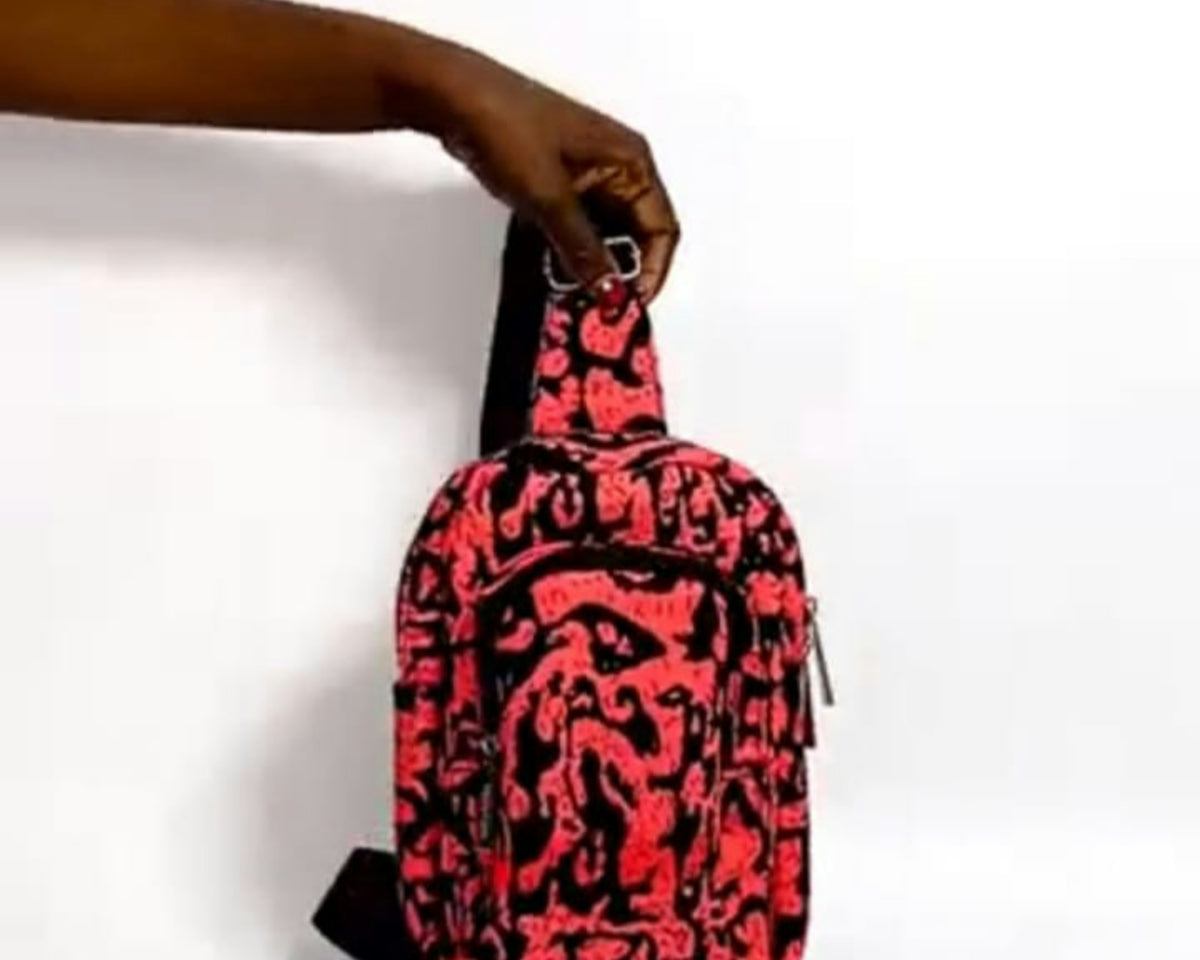 Hand holds a sling bag with a red and black pattern.