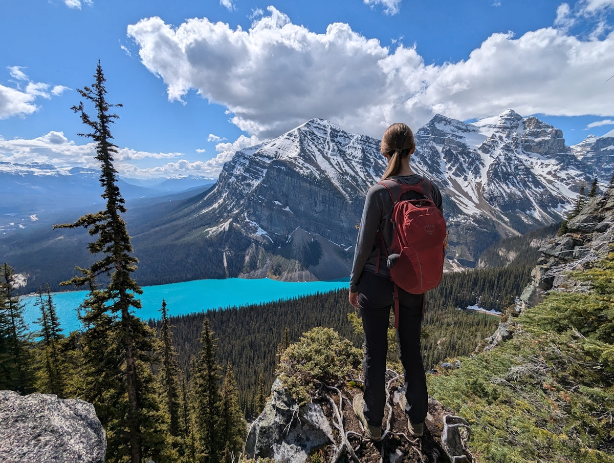 Woman with backpack overlooks turquoise lake and mountains